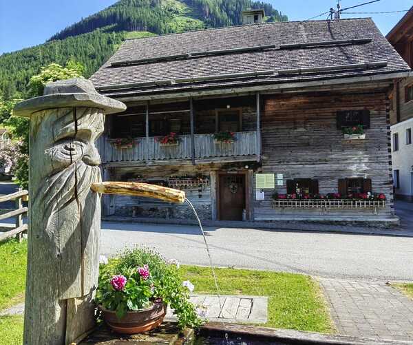 © Verein zur Bewahrung des alten Wissens der Sölktäler Ein Holzbrunnen, dahinter das Mesnerhaus